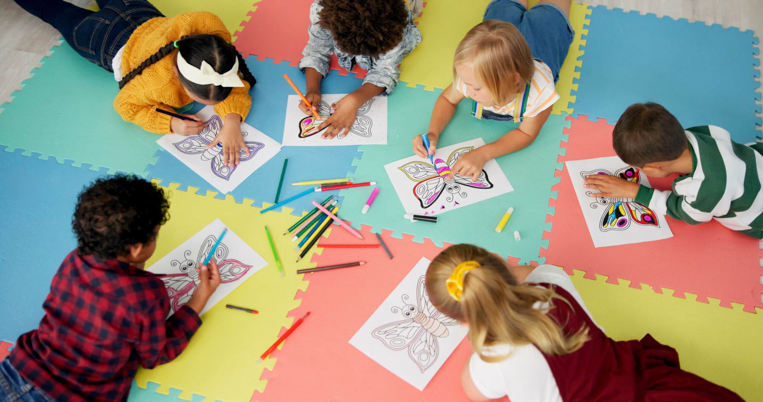 Children coloring butterfly pictures together on a classroom floor